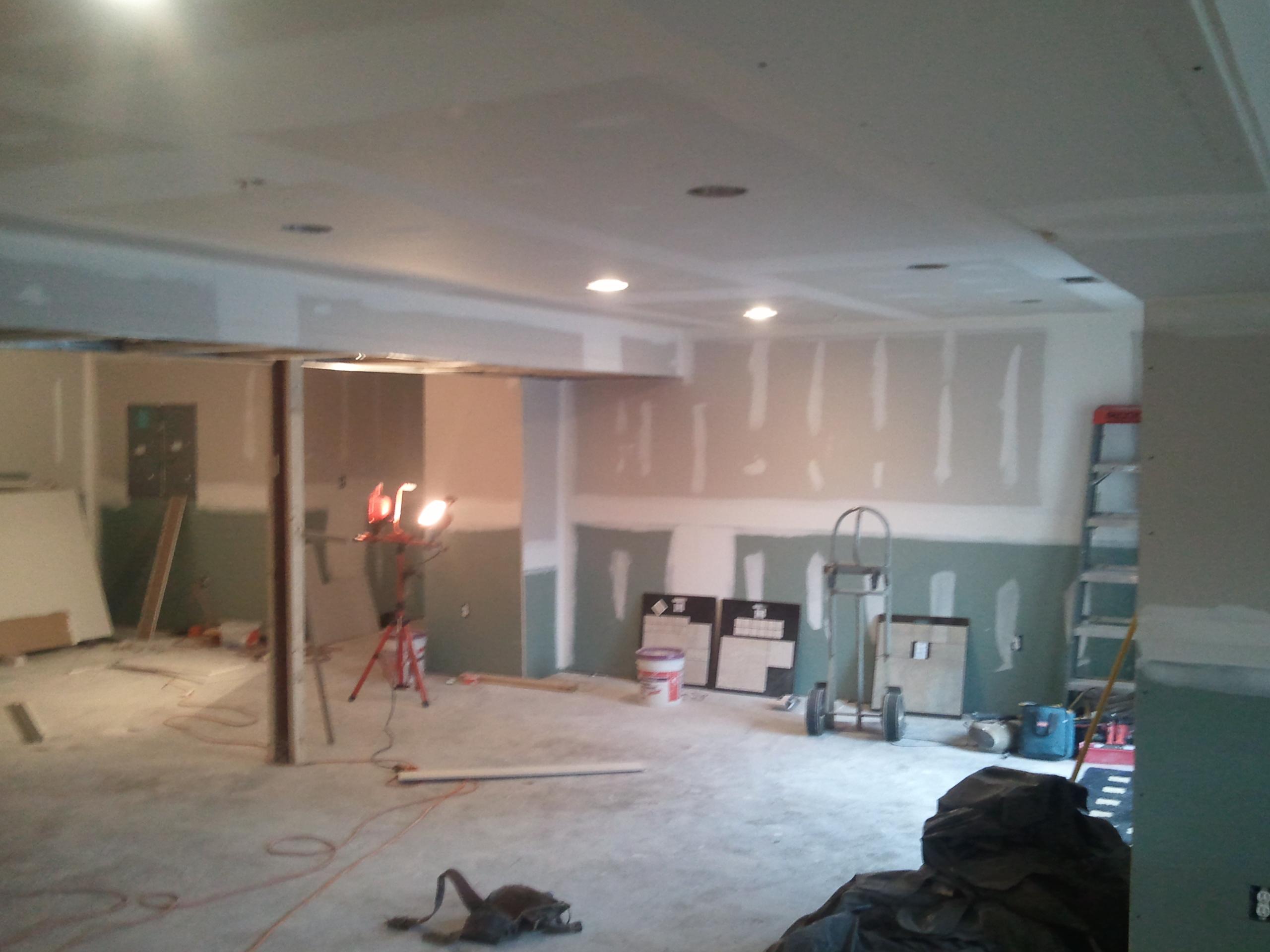Unfinished basement under construction with drywall installation, exposed framing, tools, and work lights.