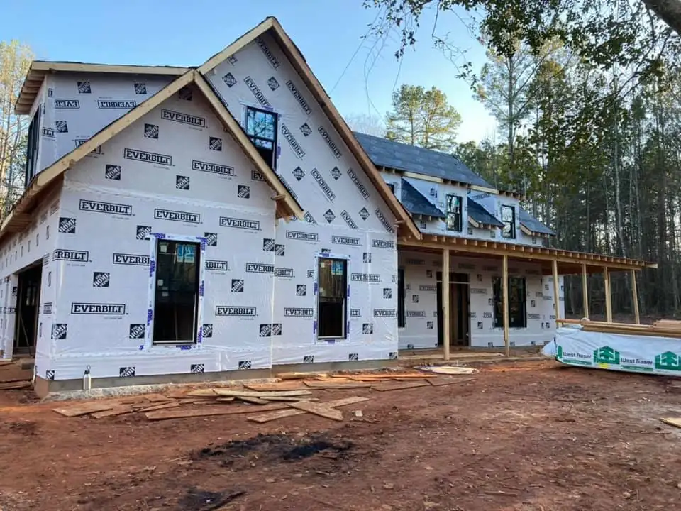 New home construction wrapped in Everbilt house wrap with framing, windows installed, and exterior porch structure in progress.