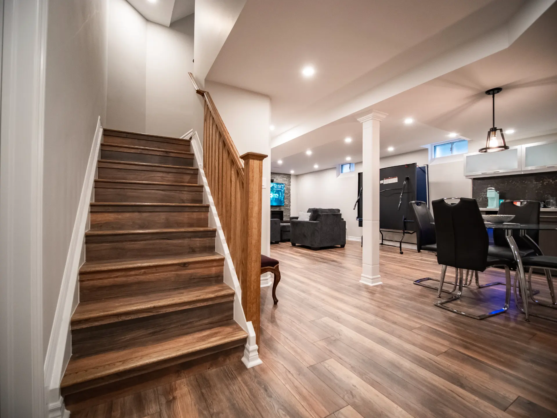Modern finished basement with wood flooring, entertainment area, and staircase.