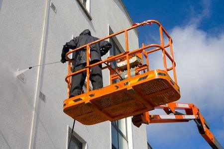 Worker on lift cleaning building façade with pressure washer.