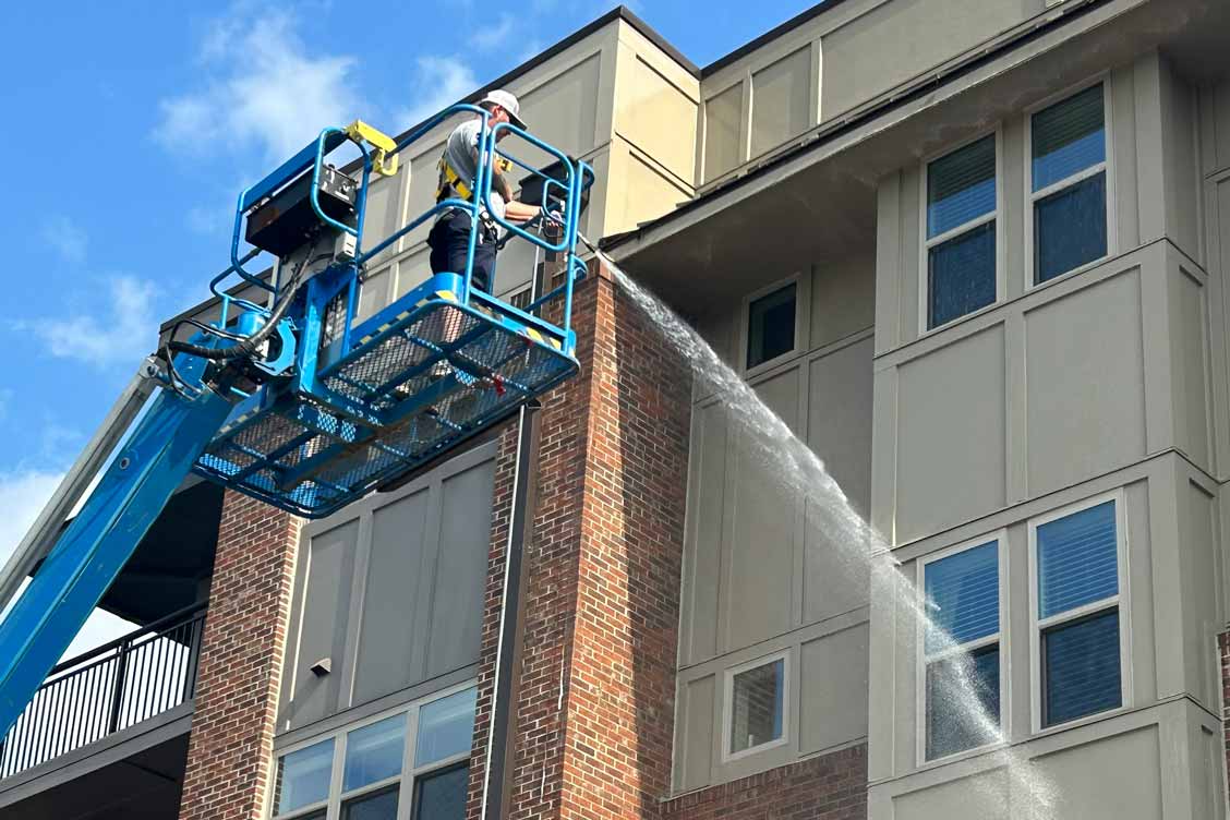 Worker using lift to pressure wash exterior brick building.