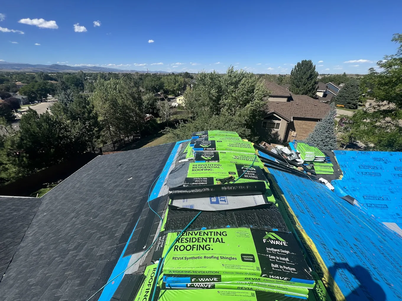 Stacks of architectural roofing shingles and underlayment materials on a residential roof during a roof replacement project.