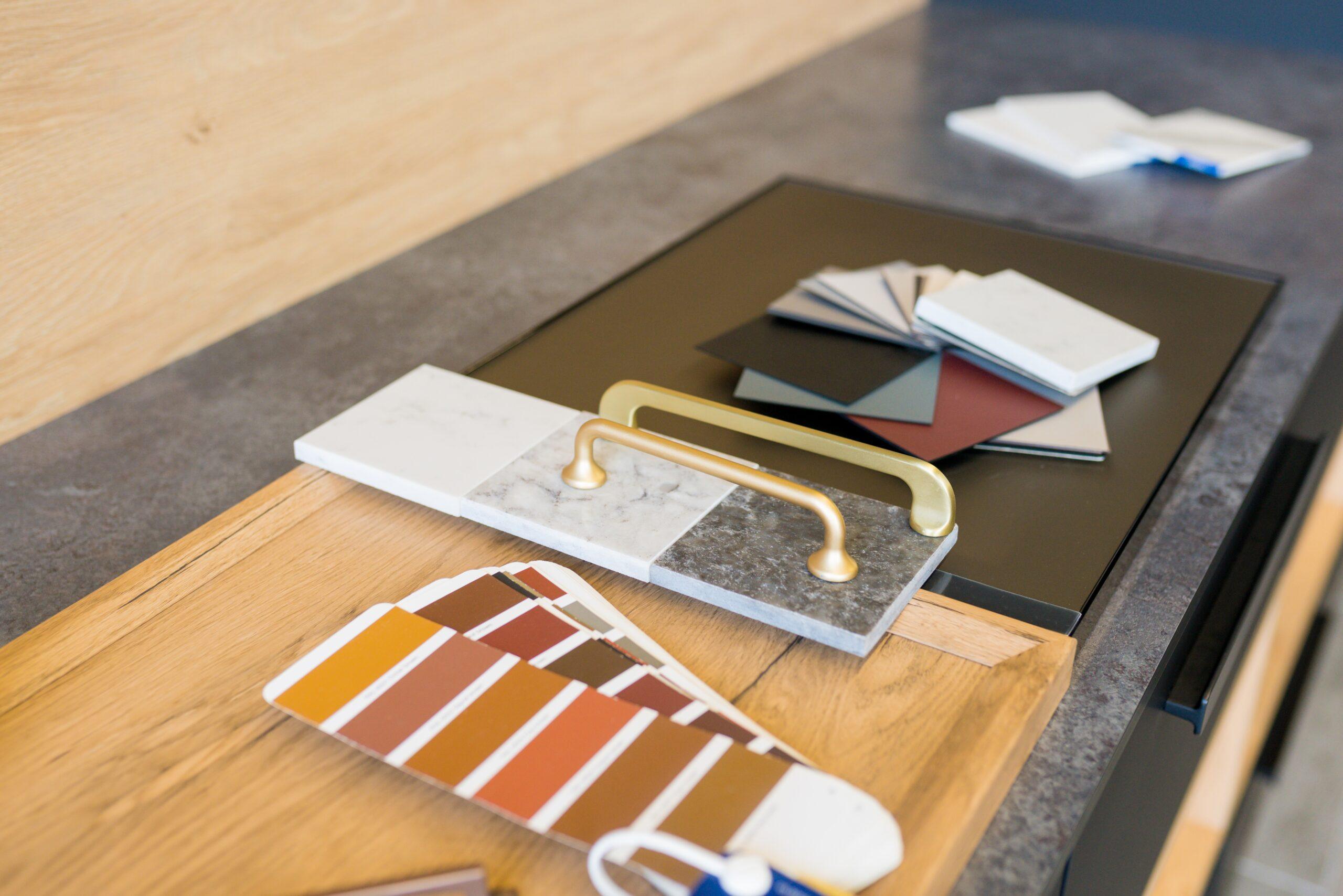 Close-up of kitchen design materials including cabinet handles, countertop samples, and color swatches arranged on a wooden surface.