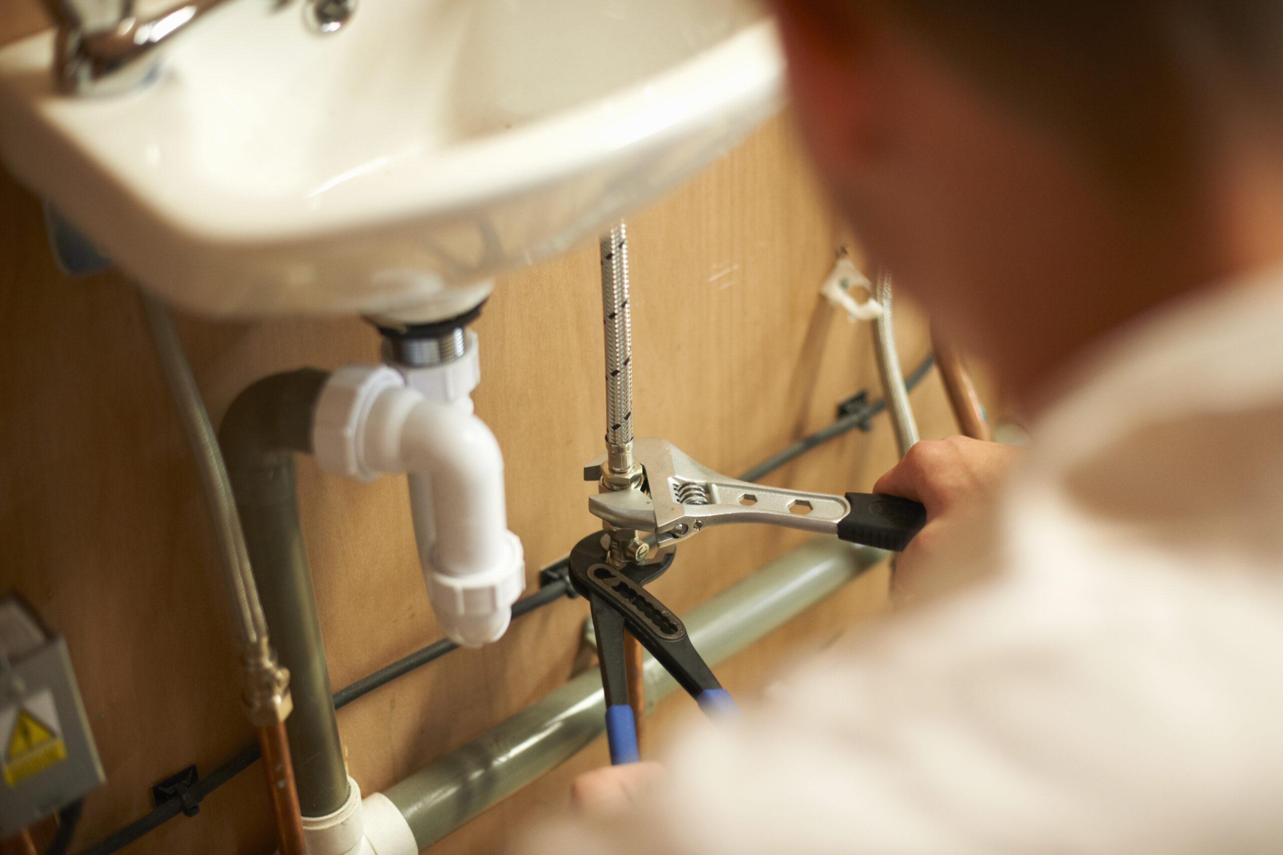 Technician performing plumbing maintenance under a sink using adjustable wrench and pliers